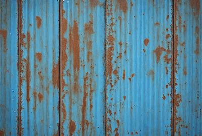 The primary subject of the image is a blue wall with rust stains on it. The setting is a room with a blue wall, and the visual style is a photo. The dominant colors are blue and rust, creating a mood of aged and worn-out appearance.