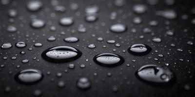The primary subject of the image is a close-up of water droplets on a black surface. The setting is a dark background, and the visual style is a photo. The colors in the image are predominantly black and white, with the water droplets appearing as small circles. The overall atmosphere of the image is moody and dramatic.