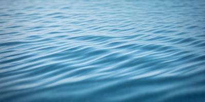The primary subject of the image is a large body of water, which appears to be a blue ocean. The setting is a vast expanse of water, with no visible land or other objects in the background. The visual style of the image is a close-up of the water, showcasing the waves and the depth of the ocean. The colors and mood of the image are predominantly blue, creating a serene and calming atmosphere.
