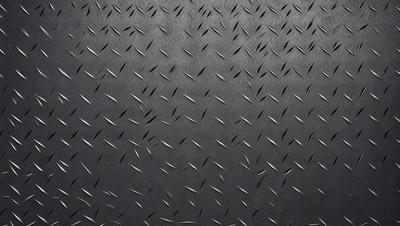 The primary subject of the image is a close-up of a black surface with a pattern of metal spikes. The setting is a dark room, and the visual style appears to be a combination of a photo and a digital art or illustration. The dominant colors are black and silver, creating a moody and dramatic atmosphere.
