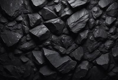The primary subject of the image is a large pile of black rocks. The setting is a dark room, possibly a cave or a black and white photo. The visual style is a black and white photo, giving the image a classic and dramatic appearance. The dominant colors are black, and the overall atmosphere is moody and mysterious.