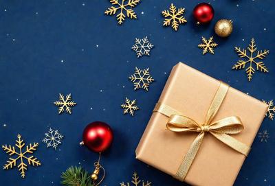 The primary subject of the image is a gold bowed ribbon, which is placed on a blue surface. The setting is a winter scene with snowflakes and Christmas ornaments in the background. The visual style is a combination of photo and digital art, creating a festive and warm atmosphere. The dominant colors are gold, blue, and white, with the snowflakes adding a touch of coldness to the overall mood.