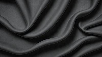 The primary subject of the image is a close-up of a black fabric, possibly a piece of clothing or a curtain. The setting is a dark background, which emphasizes the fabric's texture and pattern. The visual style appears to be a photo, as it captures the details of the fabric. The colors and mood of the image are predominantly dark, with the black fabric being the main focus.
