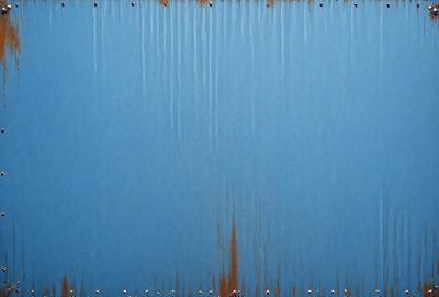 The primary subject of the image is a blue metal surface with rust stains. The setting is an outdoor environment, and the visual style appears to be a photo. The dominant colors are blue and rust, creating a mood of aged and weathered material.