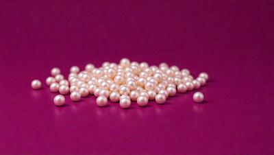 The primary subject of the image is a pile of pearls. The pearls are white and are arranged on a purple surface. The setting appears to be a table or a countertop. The visual style of the image is a close-up of the pearls, showcasing their details and beauty. The colors and mood of the image are predominantly purple and white, creating a sense of elegance and sophistication.