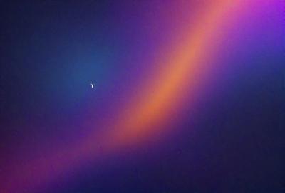 The primary subject of the image is a moon, which is located in the upper left corner of the scene. The setting is a purple sky, creating a unique and visually striking backdrop. The visual style of the image is a combination of photo and digital art, as it appears to be a photo of a painting or a digital artwork. The dominant colors in the image are purple and blue, giving the scene a calm and serene atmosphere.