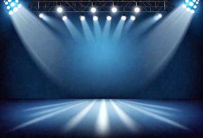 The primary subject of the image is a stage with a blue background. The stage is illuminated by a series of spotlights, creating a dramatic and theatrical atmosphere. The setting is a stage, and the visual style is a photo. The dominant colors are blue and white, with the blue background and the white spotlights creating a striking contrast. The overall mood of the image is one of drama and performance.