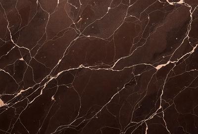 The image features a brown marble wall with a pattern of swirls and lines. The wall appears to be made of stone, giving it a natural and textured appearance. The primary subject of the image is the marble wall, which serves as the main focus of the scene. The setting is indoors, likely in a room or a building with a stone or marble theme. The visual style of the image is a close-up of the marble wall, showcasing its intricate patterns and textures. The colors and mood of the image are warm and earthy, with the brown marble wall creating a sense of natural beauty and elegance.