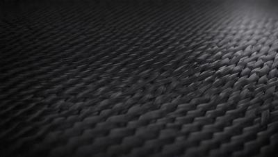 The primary subject of the image is a close-up of a black, woven fabric. The setting is a dark background, which contrasts with the fabric. The visual style is a black and white photo, giving the image a classic and timeless appearance. The colors and mood are predominantly dark and moody, with the black fabric and the dark background creating a sense of depth and mystery.