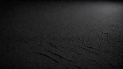 The primary subject of the image is a black leather surface. The setting is a dark room, and the visual style is a close-up of the leather surface. The colors and mood of the image are predominantly dark and moody, with the black leather creating a dramatic and intense atmosphere.