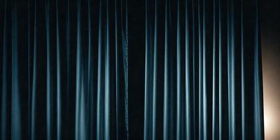 The primary subject of the image is a curtain, which is the main object in the scene. The curtain is blue and is hanging in front of a black background. The visual style of the image is a photo, and the dominant colors are blue and black. The overall atmosphere of the image is dramatic and moody.