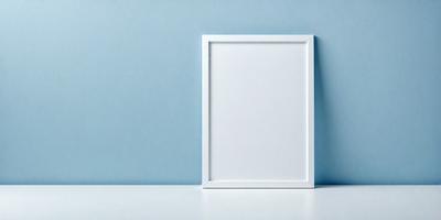 The primary subject of the image is a white picture frame, which is placed on a white surface. The setting is a blue wall, creating a contrasting backdrop for the picture frame. The visual style is a photo, capturing the details of the white frame and the blue wall. The colors and mood of the image are predominantly white and blue, giving it a clean and calm atmosphere.