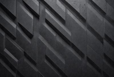 The primary subject of the image is a black and white photo of a wall with a pattern of triangles. The setting is a black background, and the visual style is a close-up of the wall. The dominant colors are black and white, creating a stark and minimalist atmosphere.