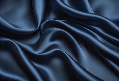 The primary subject of the image is a blue fabric, which appears to be a piece of silk. The setting is a dark background, which contrasts with the blue fabric. The visual style is a close-up of the fabric, showcasing its texture and details. The colors and mood of the image are predominantly dark and moody, with the blue fabric being the main focal point.