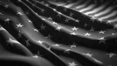 The primary subject of the image is a large, close-up view of the American flag. The flag is made up of many stars and stripes, and it is displayed in a black and white color scheme. The setting is a black background, which emphasizes the flag's design and colors. The visual style is a high-quality photo, capturing the intricate details of the flag. The overall atmosphere of the image is patriotic and symbolic, representing the United States' national identity.