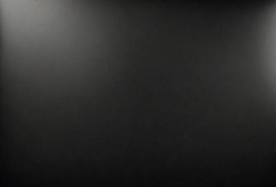 The primary subject of the image is a black background with a white light source. The setting is a dark room, and the visual style is a black and white photo. The colors and mood of the image are predominantly dark and moody, with the white light source creating a stark contrast against the black background.