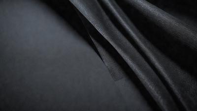 The primary subject of the image is a piece of black fabric. The setting is a dark room, and the visual style appears to be a close-up of the fabric. The colors and mood of the image are predominantly dark and moody, with the black fabric as the main focus.