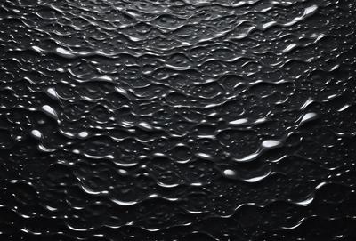 The primary subject of the image is a close-up of a black surface with water droplets on it. The setting is a dark background, and the visual style appears to be a photo of the water droplets. The colors are predominantly black, and the overall atmosphere is moist and reflective.