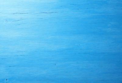 The primary subject of the image is a blue wooden surface, which appears to be a wooden table or a wall. The setting is a room with a blue color scheme, creating a calm and serene atmosphere. The visual style is a close-up of the wooden surface, showcasing its texture and details. The colors and mood of the image are predominantly blue, giving it a soothing and tranquil appearance.