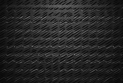 The primary subject of the image is a close-up of a black metal surface, possibly a grate or a piece of armor. The setting is a dark room, and the visual style appears to be a photo or a digital artwork. The dominant colors are black and grey, creating a moody atmosphere.