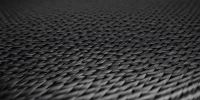 The primary subject of the image is a close-up of a black woven fabric. The setting is a black background, which provides a stark contrast to the fabric. The visual style is a detailed, up-close view of the fabric, showcasing its texture and pattern. The colors in the image are predominantly black, giving the image a moody and dramatic atmosphere.