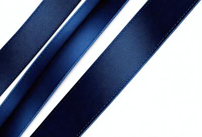 The primary subject of the image is a blue tie. The tie is prominently displayed, covering a significant portion of the image. The setting is a white background, which provides a clean and minimalistic environment for the tie to stand out. The visual style is a close-up of the tie, showcasing its details and texture. The colors and mood of the image are predominantly blue, giving the tie a calm and sophisticated appearance.