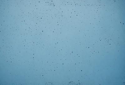 The primary subject of the image is a blue surface with black specks on it. The setting appears to be a wall or a similar surface. The visual style of the image is a close-up of the blue surface with black specks, which gives it a textured and somewhat moody appearance.