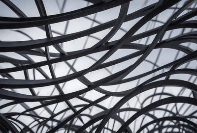 The primary subject of the image is a large, intricate metal structure with a pattern of interconnected tubes. The setting is a cloudy sky, which serves as the backdrop for the metal structure. The visual style of the image is a combination of photo and digital art, creating a unique and artistic representation of the metal structure. The dominant colors in the image are silver and gray, which contribute to the overall mood of the scene.
