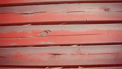 The primary subject of the image is a wooden plank with a hole in it. The setting is a wooden wall, and the visual style is a close-up of the wooden plank. The dominant colors are red and brown, giving the image a warm and rustic atmosphere.