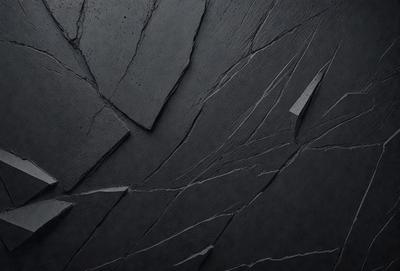 The primary subject of the image is a close-up of a black surface with a pattern of cracks and crevices. The setting appears to be a dark room, and the visual style is a black and white photo. The dominant colors are black and white, and the overall atmosphere is somewhat mysterious and intriguing.