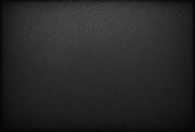 The primary subject of the image is a black background with a few white specks. The setting is a dark room, and the visual style is a black and white photo. The dominant colors are black and white, and the overall atmosphere is moody and dramatic.