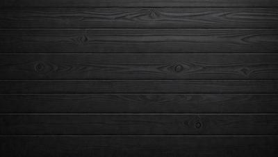 The primary subject of the image is a wooden wall. The setting is a black background, which creates a striking contrast with the wooden surface. The visual style is a close-up of the wooden wall, showcasing its texture and details. The colors and mood of the image are predominantly black, giving it a bold and dramatic appearance.