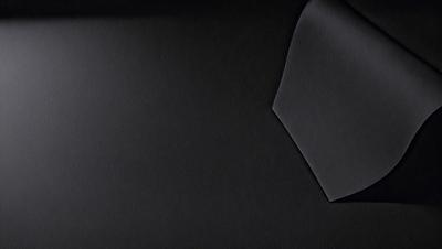 The primary subject of the image is a black piece of fabric. The setting is a dark background, which contrasts with the fabric. The visual style is a close-up of the fabric, showcasing its texture and details. The colors and mood of the image are predominantly dark, with the black fabric being the main focus.
