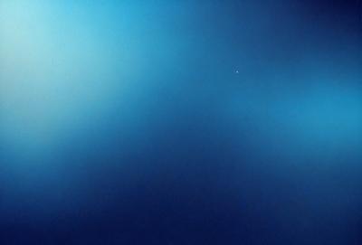 The primary subject of the image is a large, dark blue expanse of space. The setting is a vast, open area with no visible landmarks or objects. The visual style is a realistic representation of the space, with no indication of digital art or illustration. The colors and mood of the image are predominantly dark and moody, with the blue hue creating a sense of depth and vastness.