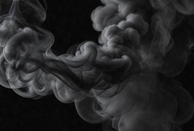 The primary subject of the image is a large, dark, and smoky cloud. The setting is a black background, which emphasizes the cloud's shape and form. The visual style is a black and white photo, giving the image a dramatic and moody atmosphere. The colors and mood of the image are predominantly dark and mysterious, with the cloud serving as the focal point of the scene.