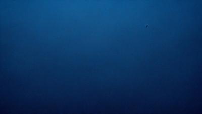 The primary subject of the image is a large, dark blue sky. The setting is a vast, open space with no visible landmarks or objects. The visual style is a natural, untouched environment. The colors and mood are predominantly dark and moody, with the blue sky serving as the main focal point.