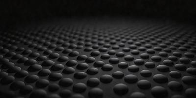 The primary subject of the image is a black surface with a pattern of small circles. The setting is a dark room, and the visual style appears to be a close-up of the black surface. The dominant colors are black and the small circles, creating a moody atmosphere.