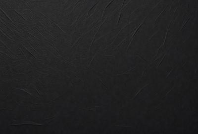 The primary subject of the image is a black leather surface. The setting is a dark room, and the visual style is a close-up of the leather surface. The colors and mood of the image are predominantly dark and moody, with the black leather serving as the focal point.