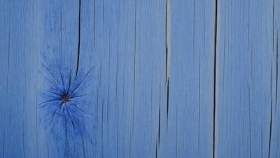 The primary subject of the image is a blue wooden wall with a hole in it. The setting is a room with a blue wooden wall, and the visual style is a photo. The dominant colors are blue and white, creating a calm and serene atmosphere.