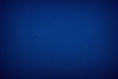 The primary subject of the image is the moon, which is visible in the sky. The setting is a dark blue sky, which creates a contrasting backdrop for the moon. The visual style of the image is a photo, capturing the moon in its natural environment. The colors and mood of the image are predominantly dark and moody, with the blue sky and the moon creating a sense of depth and tranquility.
