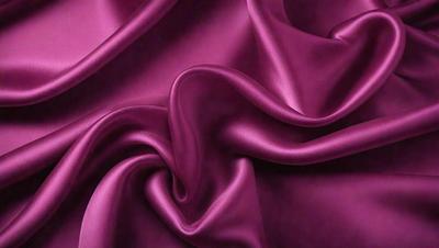 The primary subject of the image is a close-up of a purple fabric, possibly a piece of silk. The setting is a room with a purple background, which adds to the overall mood of the scene. The visual style appears to be a photo, as it captures the details of the fabric and its texture. The colors and mood of the image are predominantly purple, creating a sense of luxury and elegance.