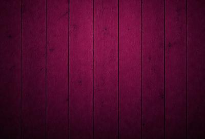 The primary subject of the image is a wooden wall with a purple color. The setting is a room with a wooden floor. The visual style is a close-up of the wooden wall, showcasing its texture and color. The dominant colors are purple and brown, creating a warm and cozy atmosphere.