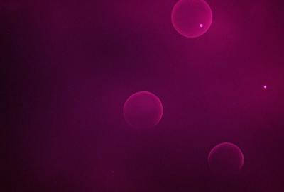 The primary subject of the image is a purple background with three pink circles floating in the air. The setting appears to be a dark, pink-lit environment. The visual style is a combination of a photo and digital art, creating a unique and artistic atmosphere. The colors and mood of the image are predominantly purple and pink, giving it a warm and inviting feel.