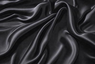 The primary subject of the image is a close-up of a black fabric, possibly a piece of clothing or a curtain. The setting is a dark room, and the visual style appears to be a photo. The dominant colors are black and grey, creating a moody atmosphere.