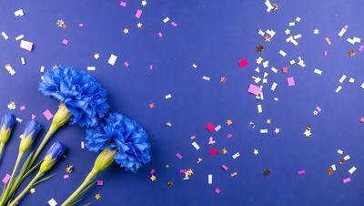 The primary subject of the image is a bouquet of blue flowers, which are the main focus of the scene. The flowers are placed on a blue surface, which serves as the setting or background. The visual style of the image is a photo, capturing the beauty of the flowers and their surroundings. The dominant colors in the image are blue and pink, creating a calm and serene atmosphere.
