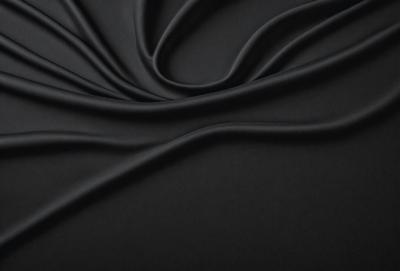 The primary subject of the image is a black fabric, which appears to be a piece of cloth or a curtain. The setting is a dark background, which contrasts with the black fabric. The visual style is a close-up of the fabric, showcasing its texture and details. The colors and mood of the image are predominantly dark, with the black fabric being the main focus.