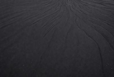 The image features a black surface with a pattern of white dots. The primary subject is a close-up of the pattern, which appears to be a sandy texture. The setting is a black background, and the visual style is a close-up of the pattern. The colors and mood of the image are predominantly black and white, creating a contrasting and visually striking scene.