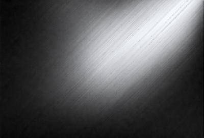 The primary subject of the image is a large, shiny, metallic surface. The setting is a dark room, and the visual style appears to be a photo. The colors and mood of the image are predominantly dark, with the metallic surface being the main focus.