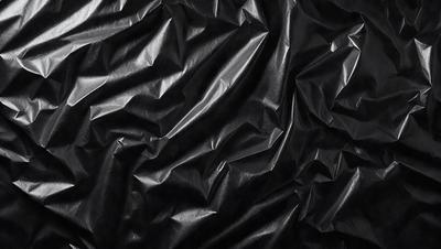 The primary subject of the image is a close-up of a black leather material, possibly a piece of clothing or a leather surface. The setting is a dark background, which emphasizes the leather material. The visual style is a close-up, focusing on the details of the leather. The colors and mood of the image are predominantly dark, with the black leather material being the main focus.