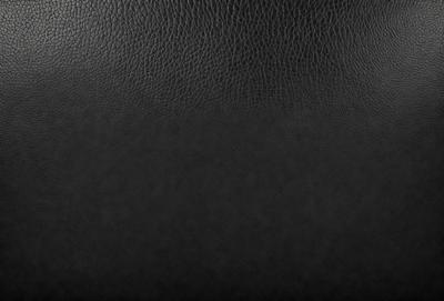 The primary subject of the image is a black leather seat. The setting is a black background, which creates a contrast with the leather seat. The visual style is a close-up of the leather seat, showcasing its texture and details. The colors and mood of the image are dark and moody, emphasizing the leather seat's richness and luxury.